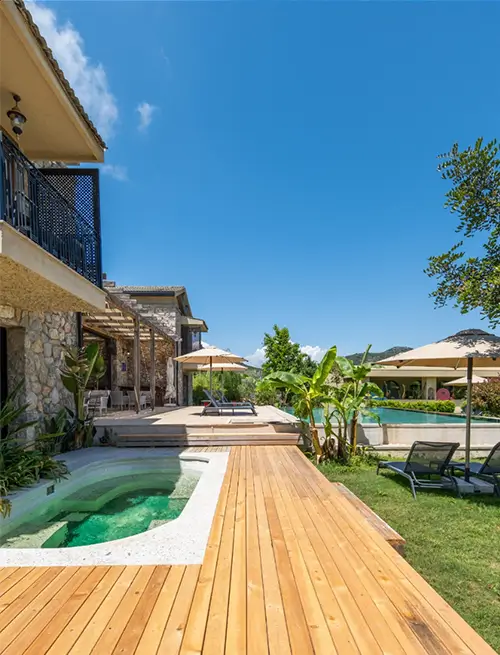 Spacious villa with wooden terrace, private pool, sun loungers, and a tranquil garden with tropical plants.